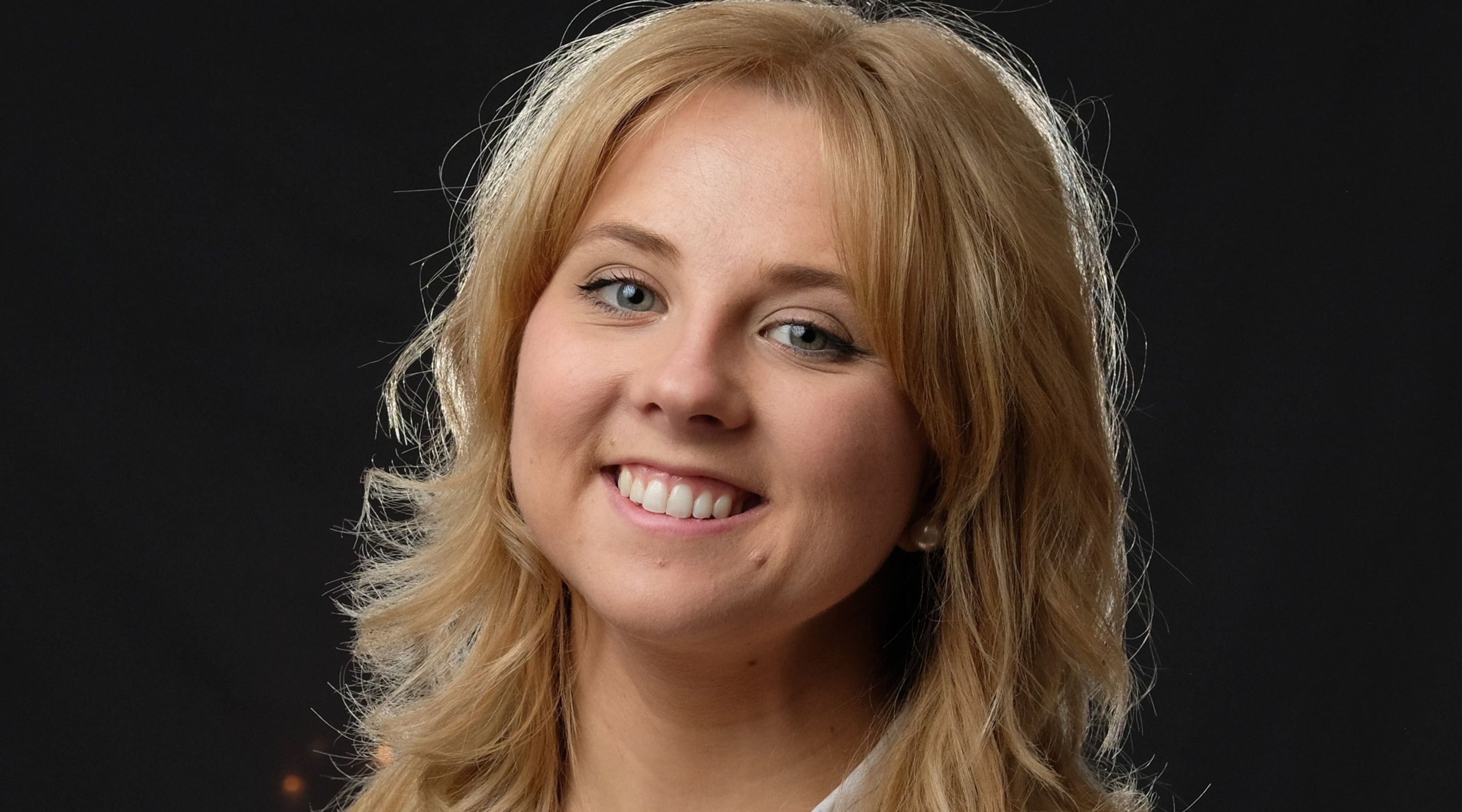 En kvinna i vit skjorta som ler mot kameran.