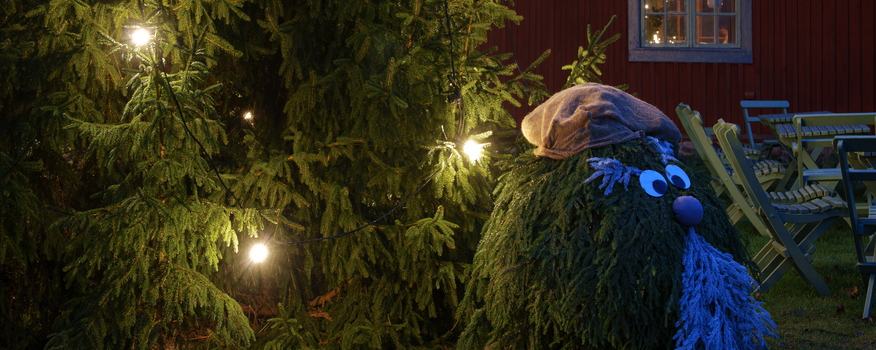 Julgran med tomte och röd byggnad i bakgrunden.