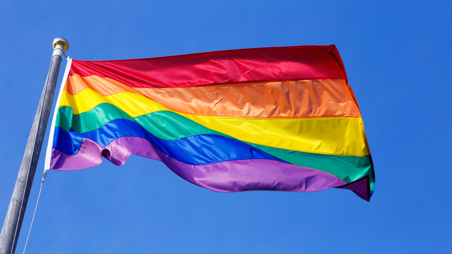 En regnbågsflagga som vajar mot en blå himmel.