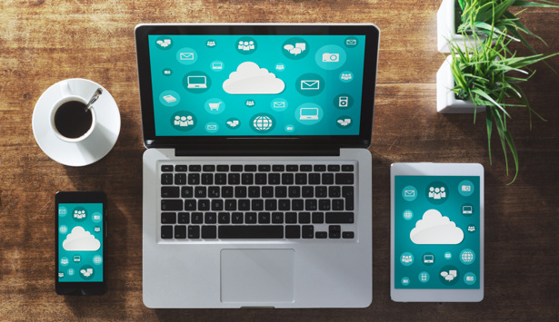 En bärbar dator, en telefon och en surfplatta som sitter på ett träbord.