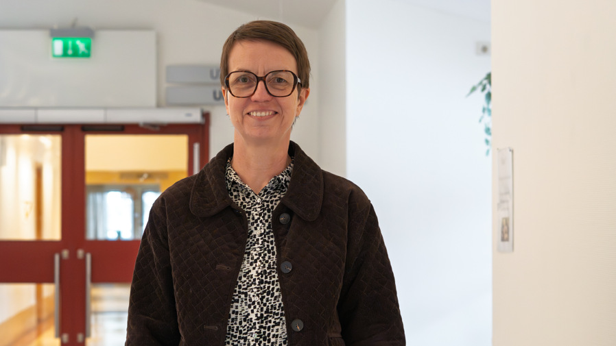 En kvinna med glasögon står i en korridor.