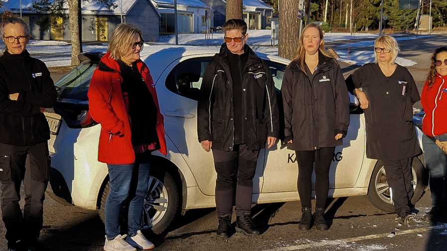 Anställda inom hemtjänsten står bredvid en av kommunens tjänstebilar.