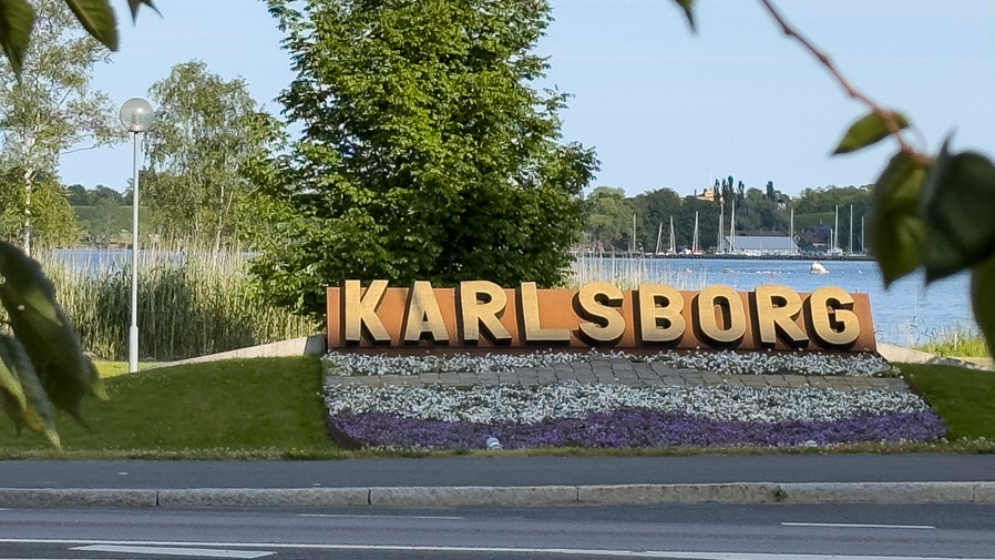 En skylt med texten "Karlsborg" med vatten i bakgrunden.