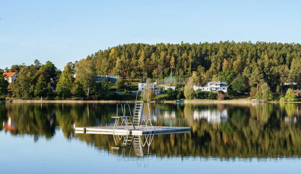 Ett hopptorn på flotte i vattnet med träd och hus i bakgrunden