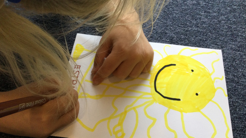 Ett barn ritar en bild av en leende sol