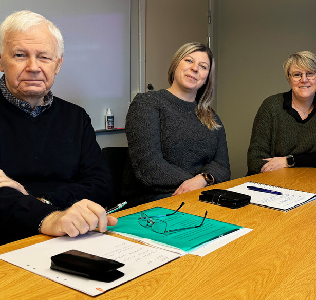 Tre personer sitter vid ett bord framför en bildskärm.