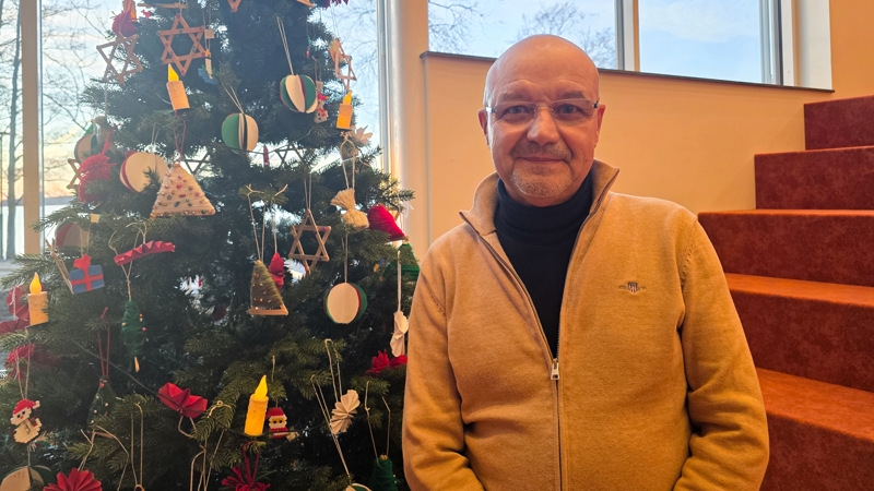 En man står inomhus framför en julgran.