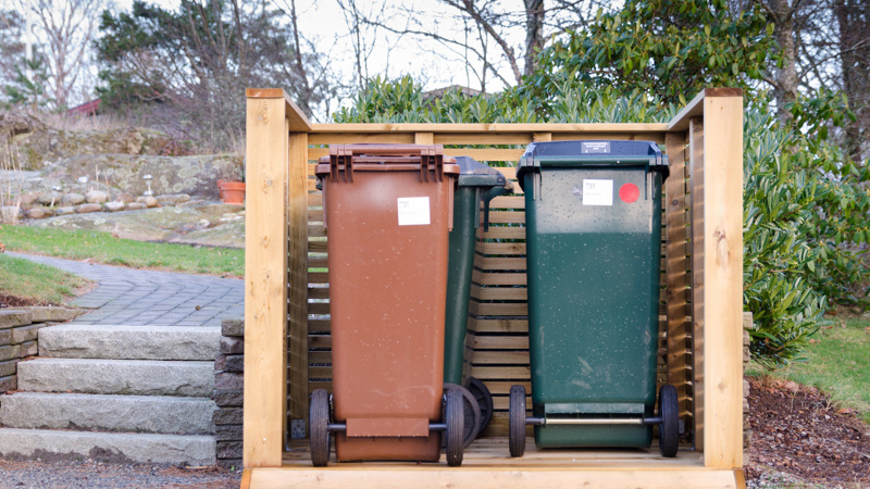 Tre soptunnor i olika färg uppställda med ett plank i trä på tre sidor.