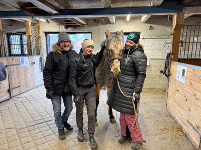Tre personer och en häst står i ett stall.