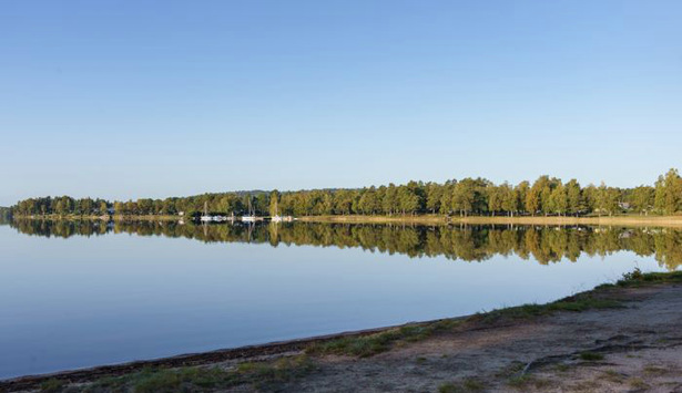 En sjö med strand  och träd i bakgrunden som speglar sig i vattnet