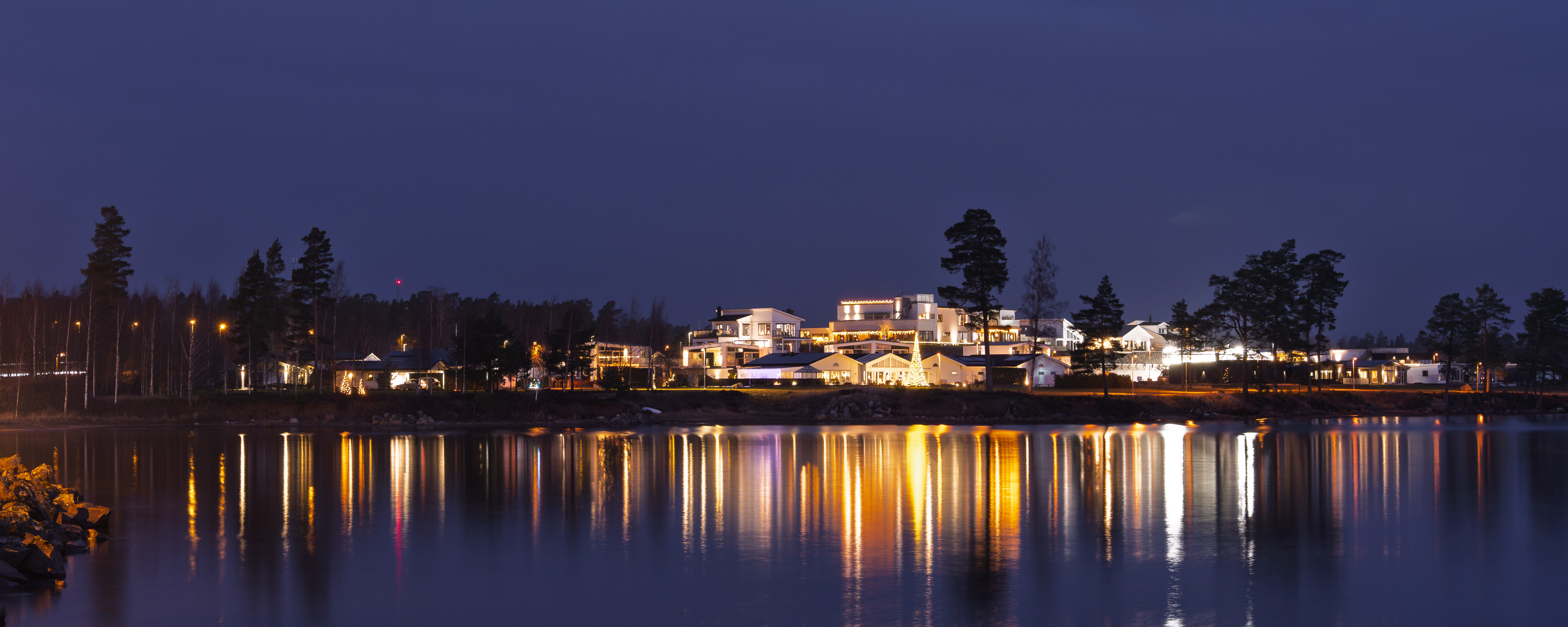 Belyst vy över Äspenäset med spegling i vattnet.