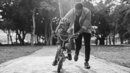 Pappa springer med sitt barn som håller på att lära sig cykla
